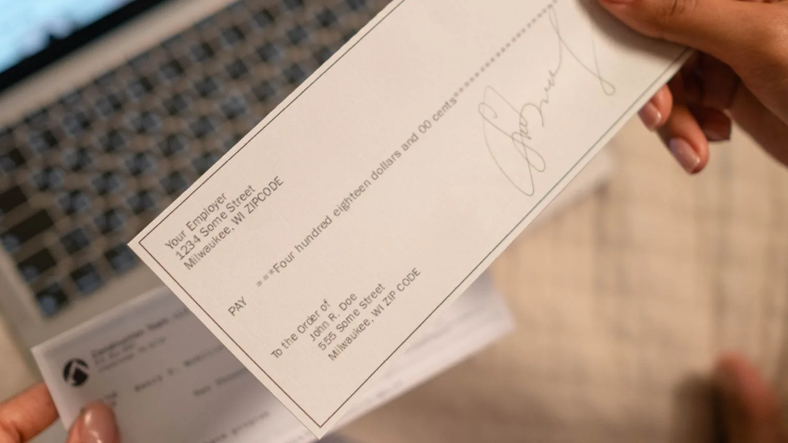 A hand holding a paper check over a laptop keyboard