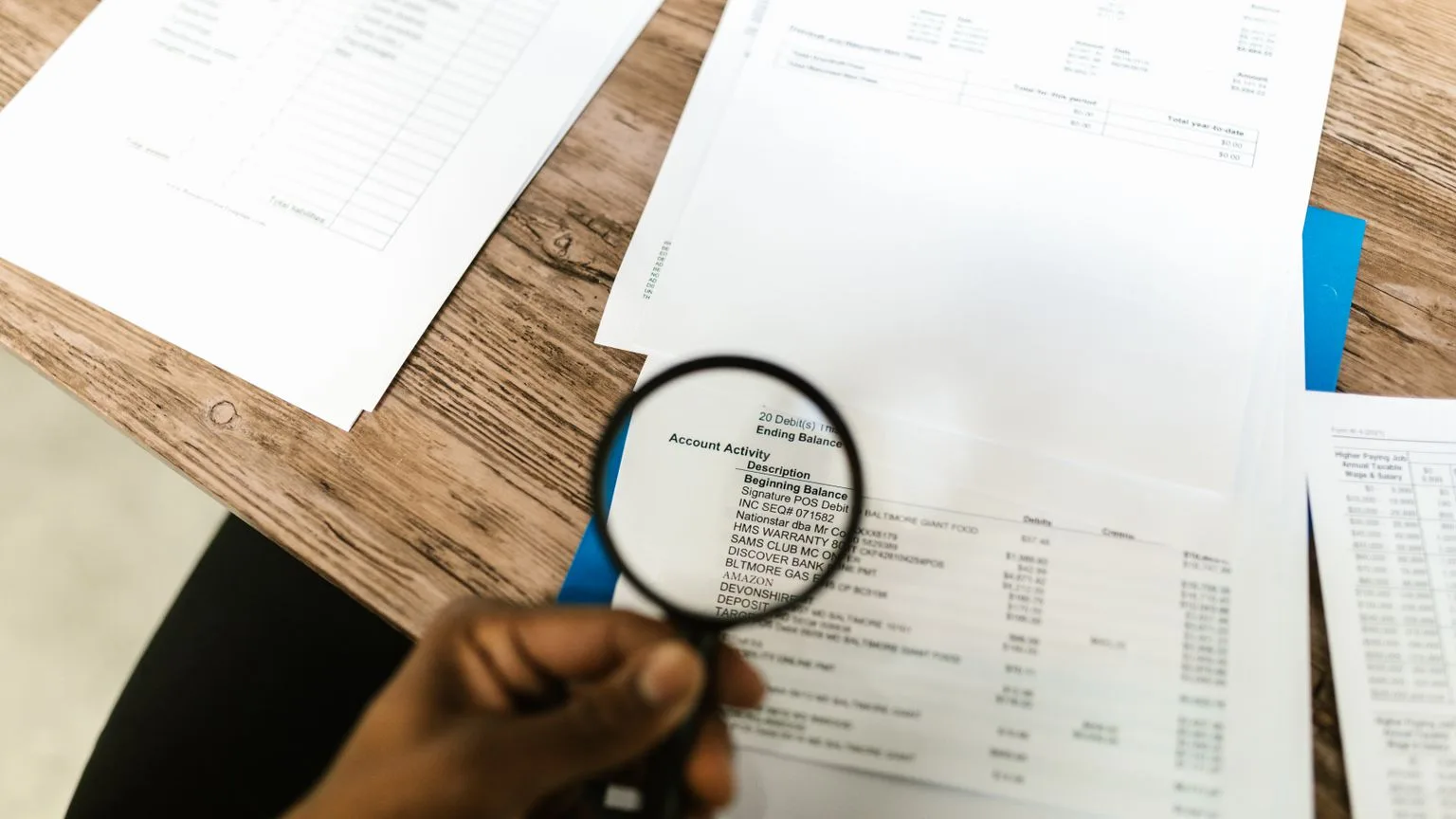 A hand holding a magnifying glass over the account activity section of a bank statement